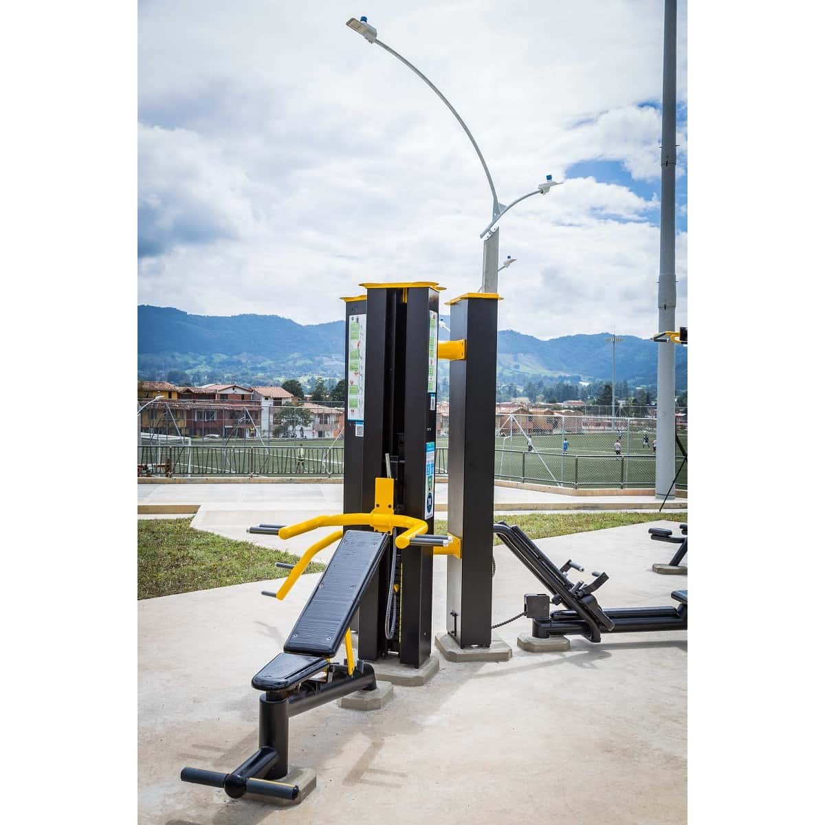 Banca abdominal inclinada de TMGYM junto a una torre de fuerza en un parque
