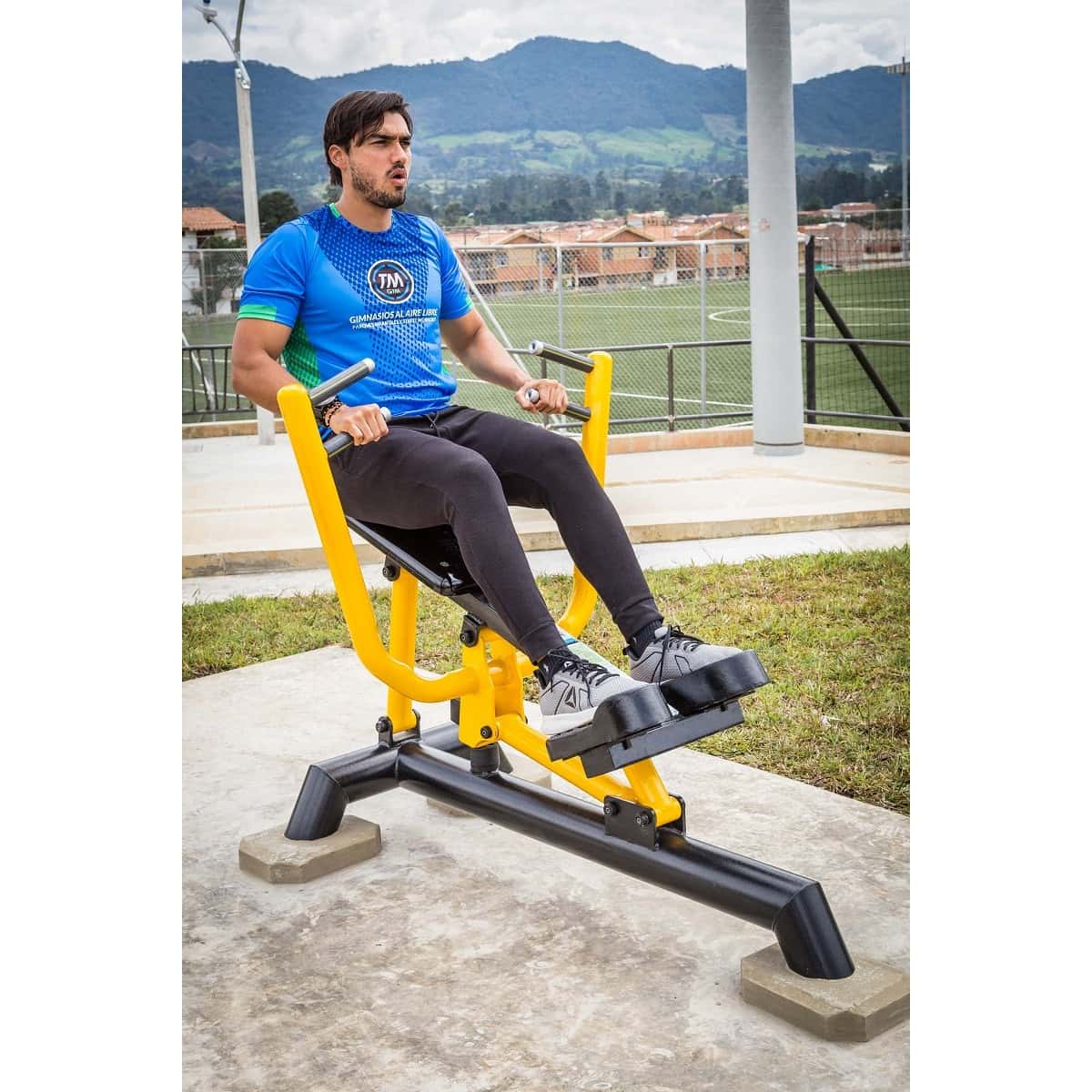 Hombre entrenando en el Remo de TMGYM con una cancha deportiva al fondo