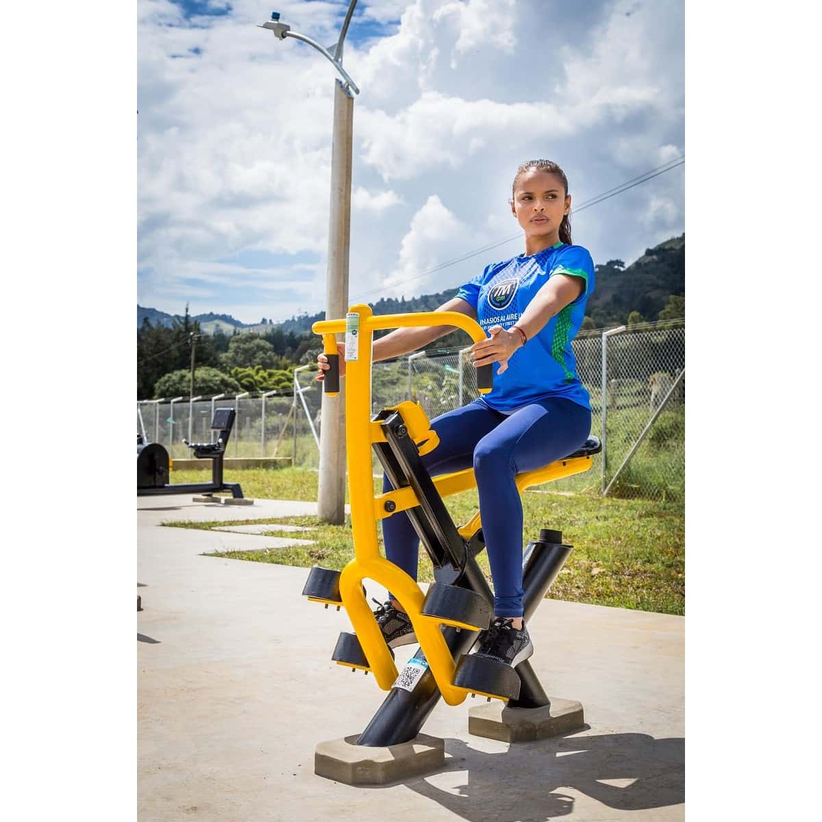 Mujer sentada en el Jinete de TMGYM entrenando en un parque con montañas al fondo