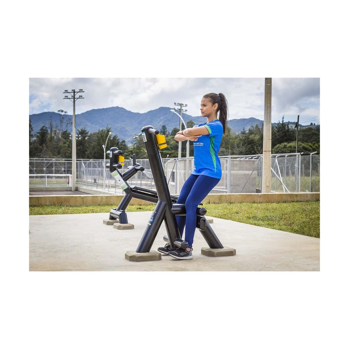 Usuaria entrenando en el calentador de piernas sissy de TMGYM, equipo negro en un parque deportivo con montañas