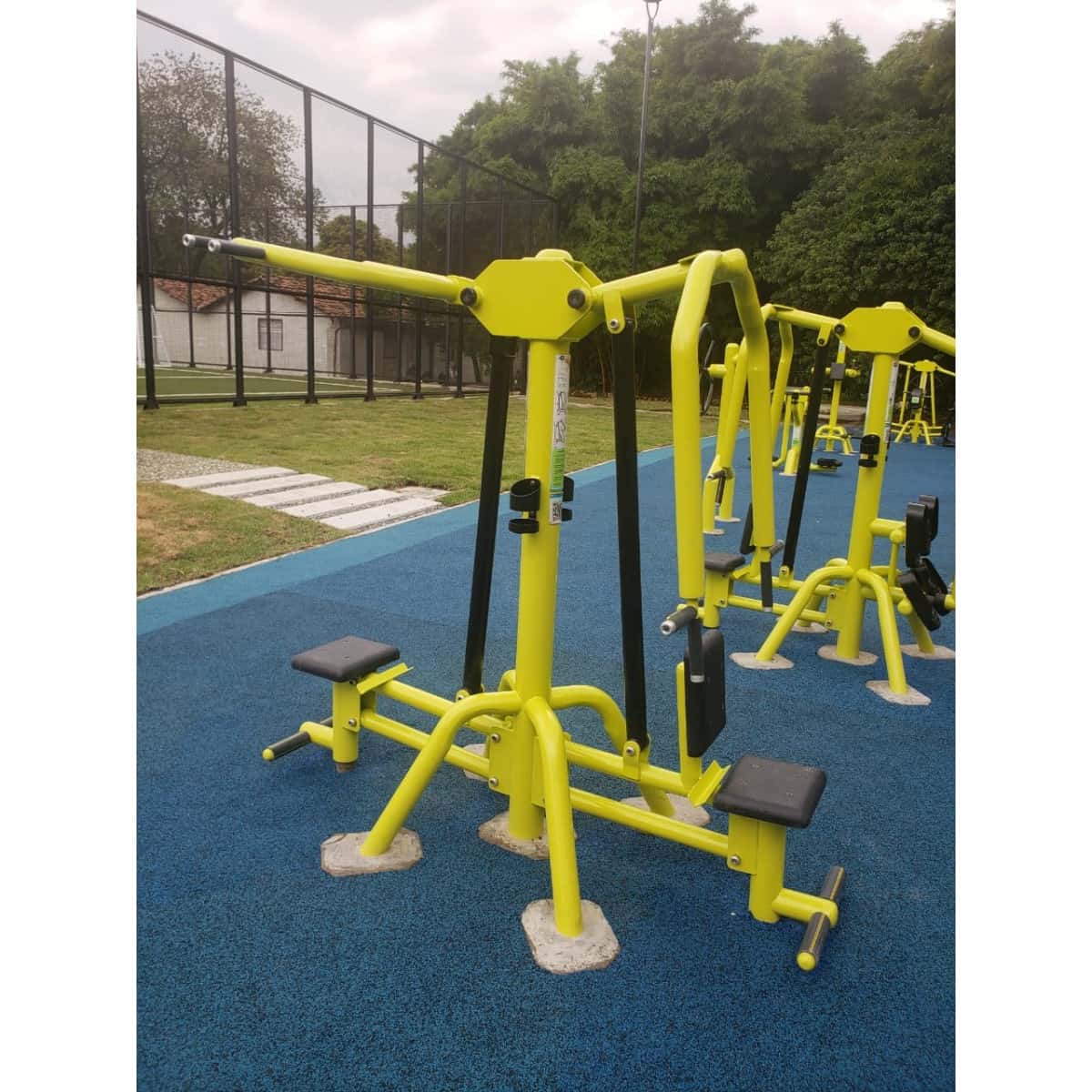 Prensa de pecho doble de TMGYM amarilla sobre piso azul junto a otros equipos