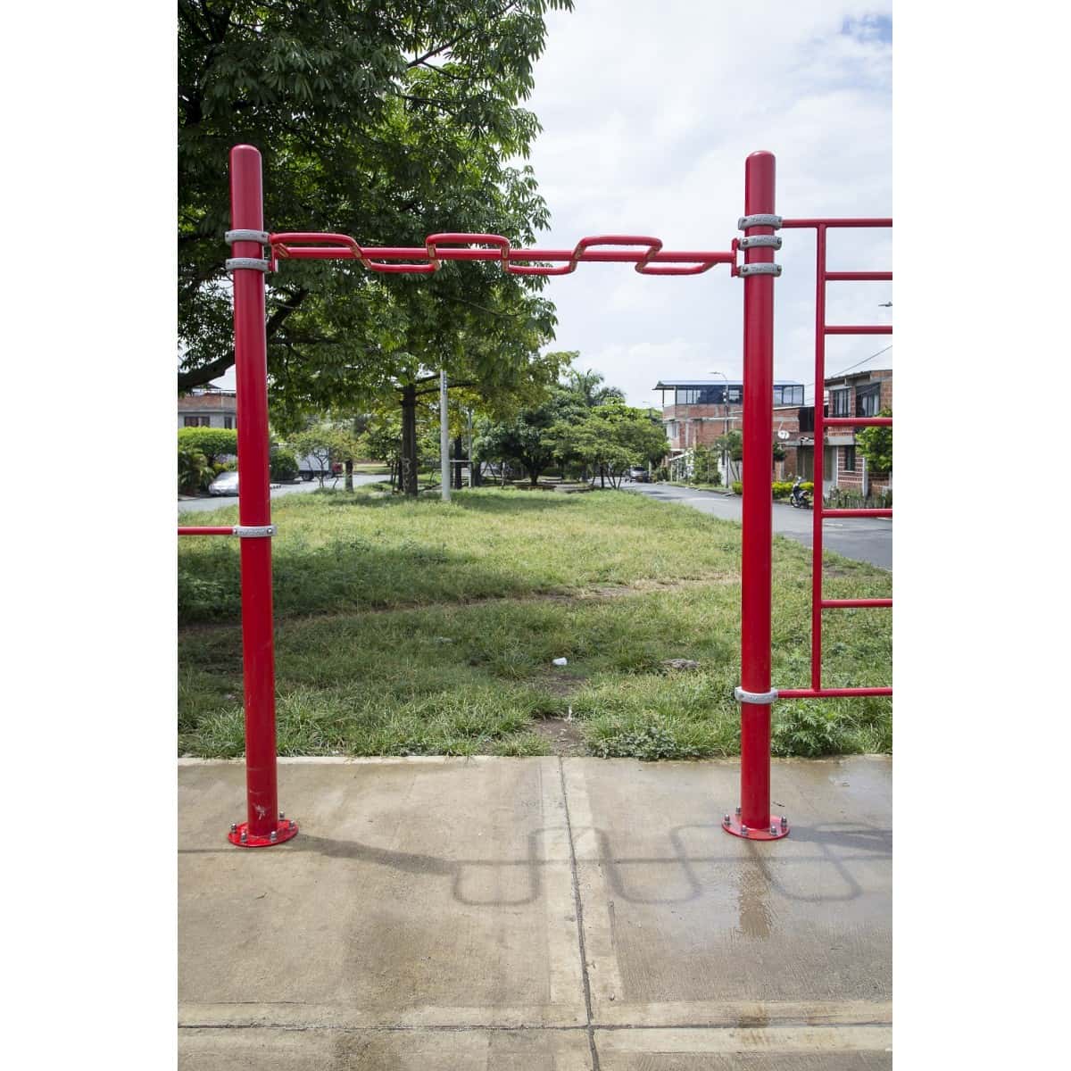 Estructura de barras rojas de calistenia de TMGYM sobre concreto con pasto