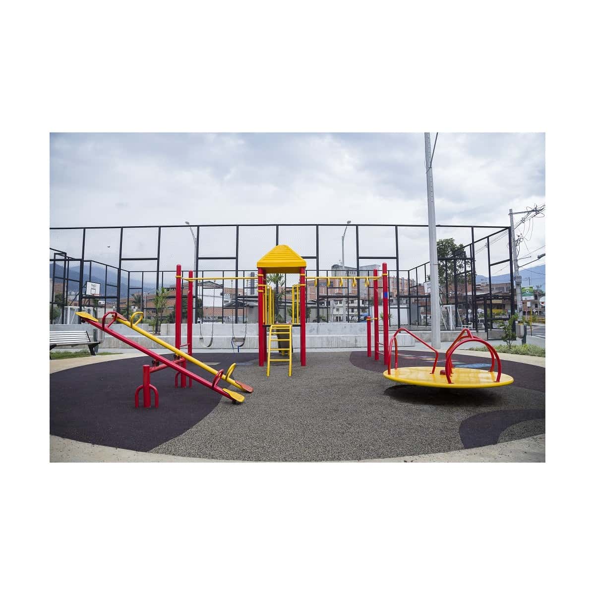 Parque infantil recreativo metálico con carrusel y balancines sobre piso oscuro