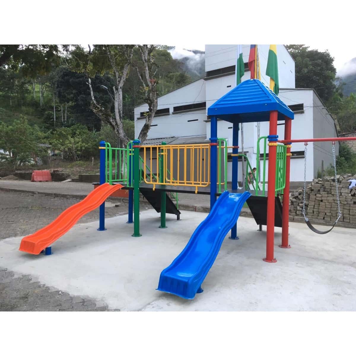 Parque infantil con techo azul y deslizaderos naranja y azul sobre piso de concreto