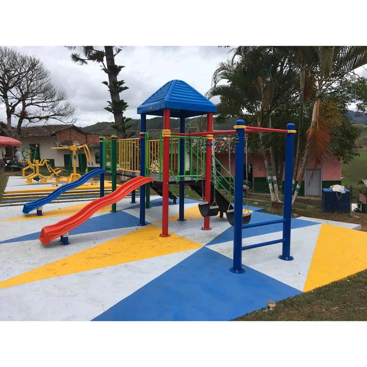 Parque infantil recreativo metálico con techo azul, deslizadero rojo y barras en un patio con piso pintado de colores