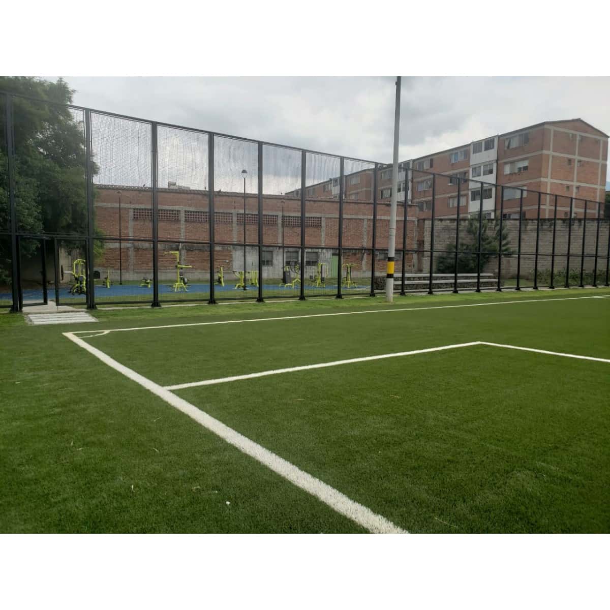 Cancha de fútbol con grama sintética y línea blanca de demarcación, cerrada con malla