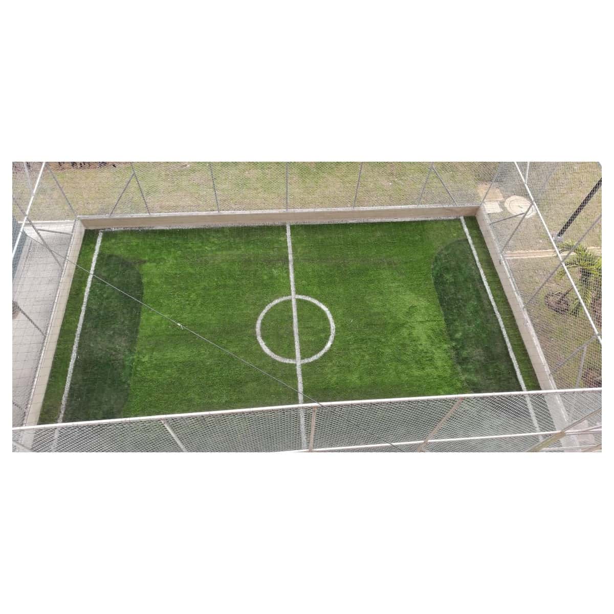 Cancha pequeña de grama sintética con círculo central, cerrada con malla