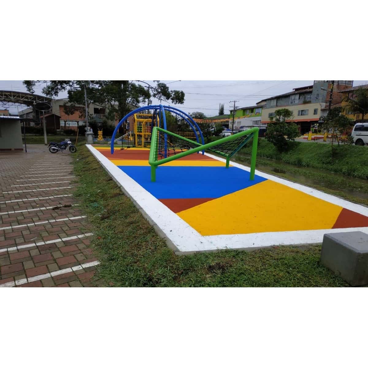 Zona de juegos infantiles con piso sintético de colores y una estructura de juego curva