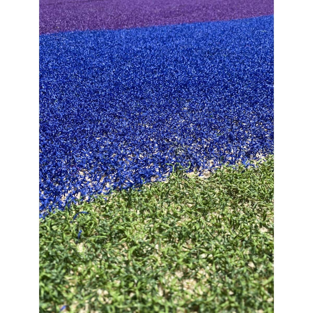 Detalle de un piso sintético azul con gránulos sobre grama