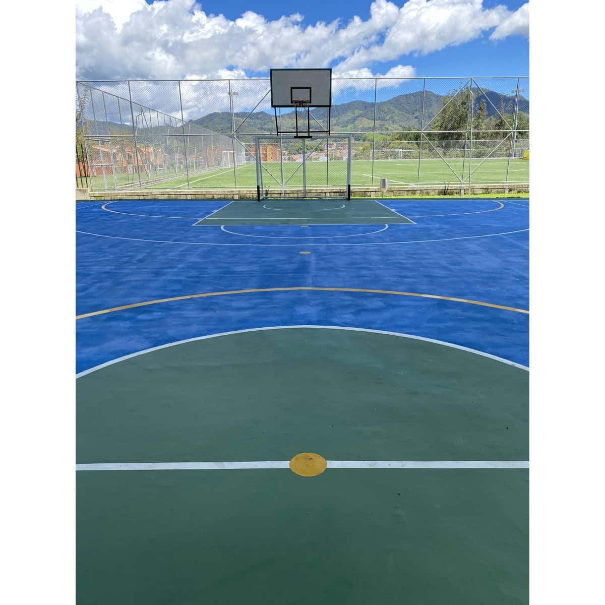 Cancha pintada en azul y verde con aro de baloncesto al fondo