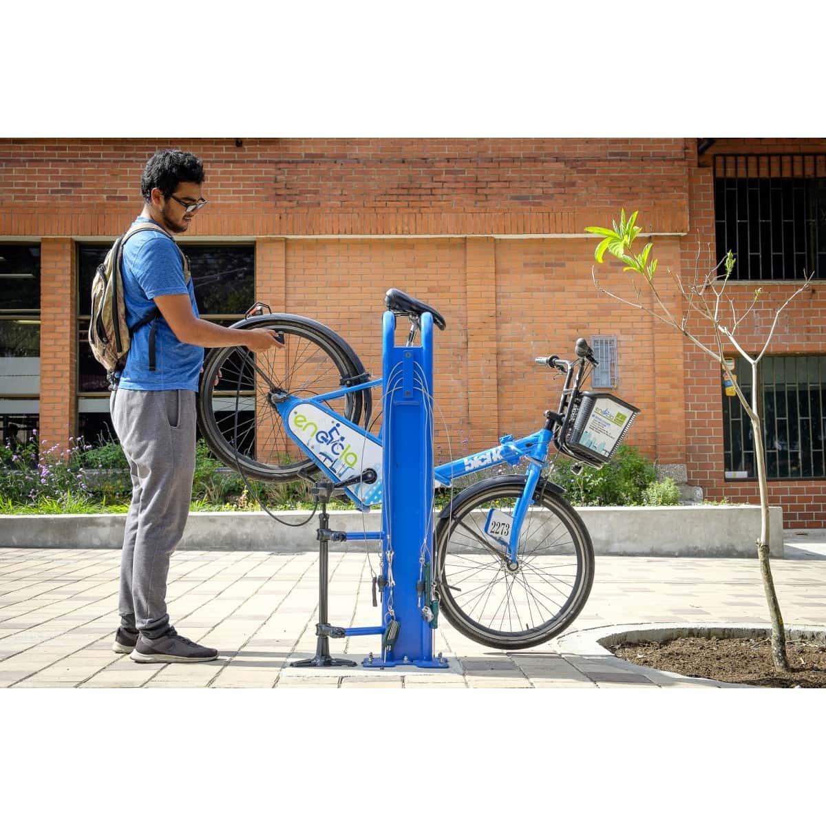 Persona ajustando una bicicleta en un bicitaller público de color azul sobre un andén urbano