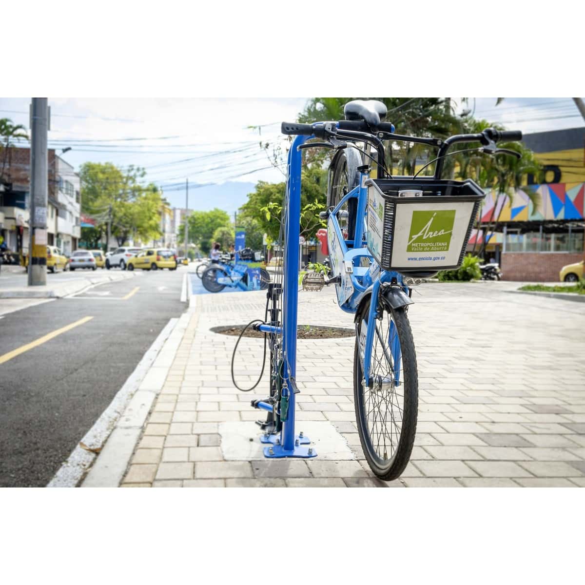Bicitaller público azul sobre un andén urbano, junto a una bicicleta