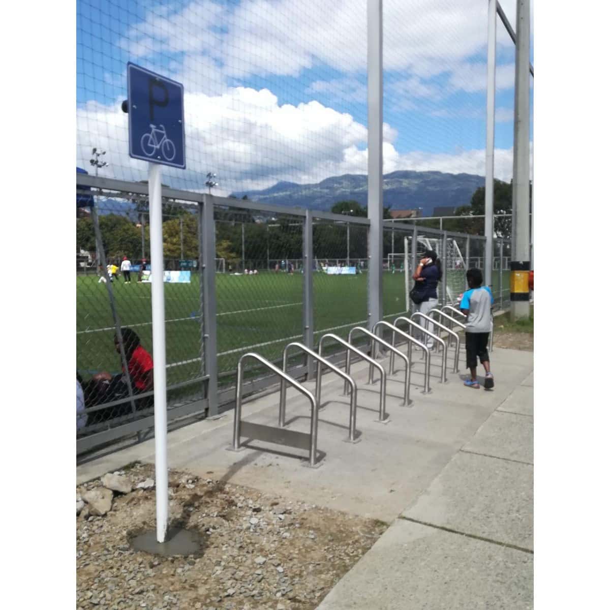 Parquearos para bicicleta junto a una señal de bicicletero frente a una cancha