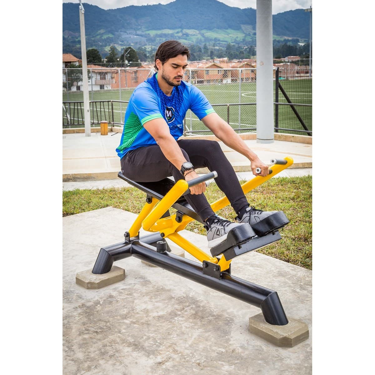 Hombre entrenando en el Remo de TMGYM, equipo de fuerza amarillo y negro en un parque deportivo