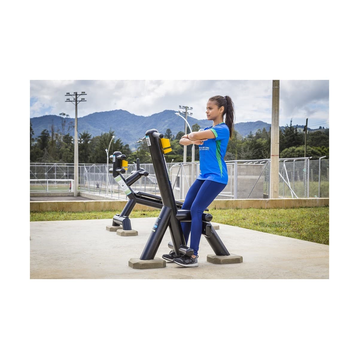 Usuaria entrenando en el calentador de piernas sissy de TMGYM, equipo negro en un parque deportivo con montañas