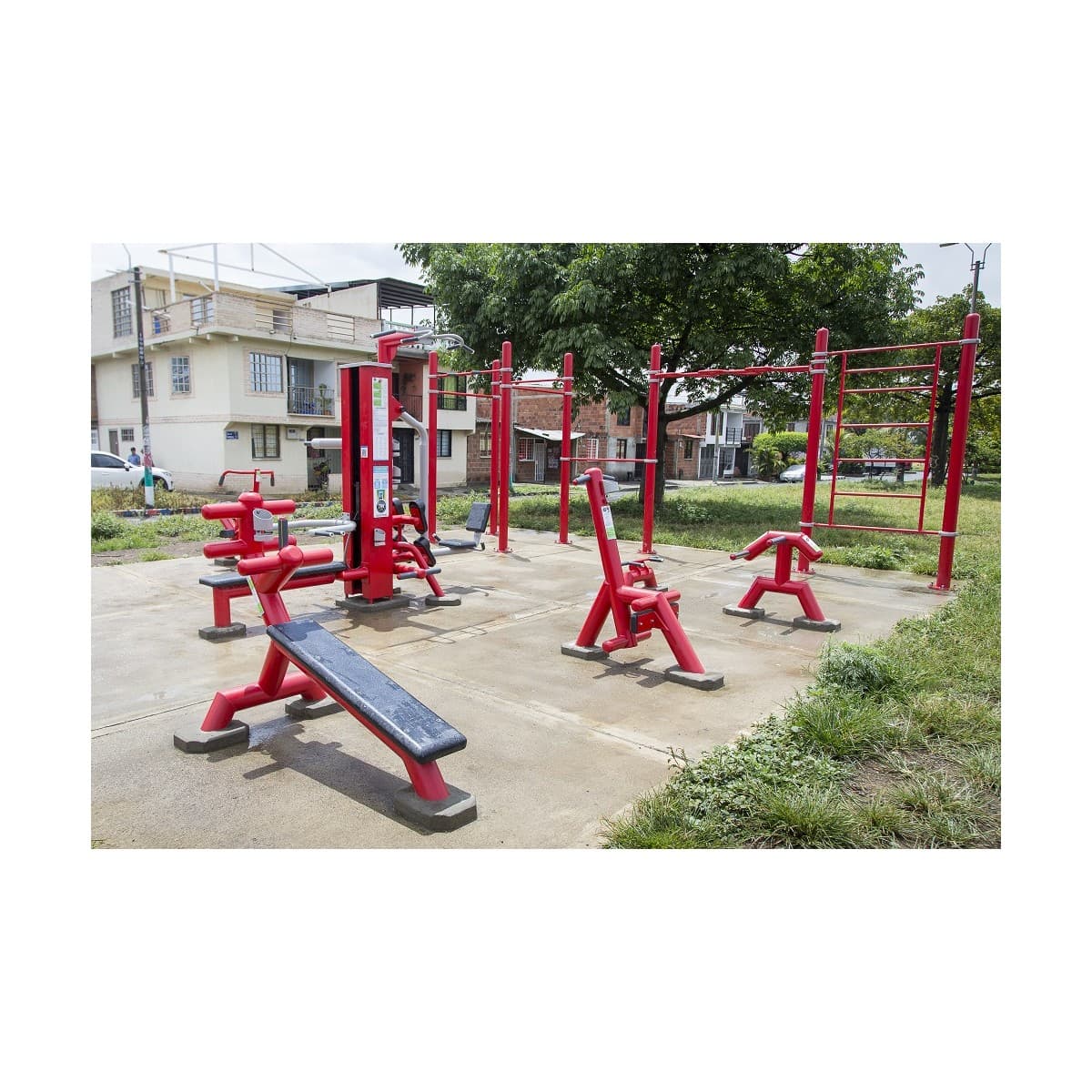 Combo TM2 de TMGYM, conjunto de equipos de gimnasio al aire libre rojos instalado en un parque con viviendas al fondo