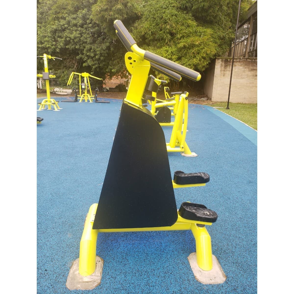 Escalador de TMGYM, equipo amarillo y negro para piernas y cardio sobre piso azul en un parque