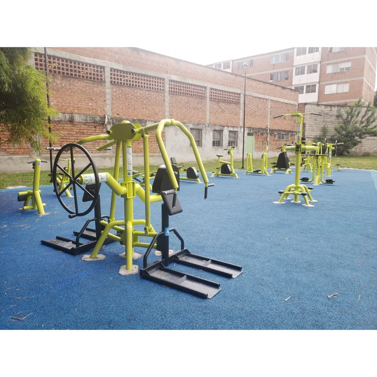 Estación multifuncional de TMGYM para movilidad reducida, equipos verdes y negros sobre piso azul en un parque