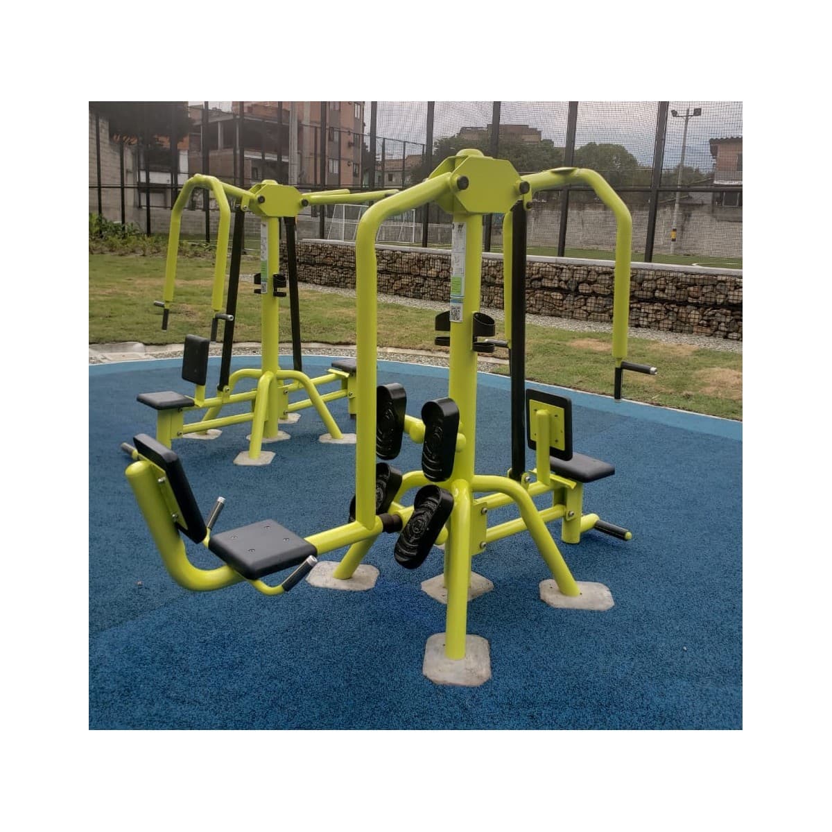 Estación de fuerza de TMGYM con prensa de piernas doble, equipos amarillos y verdes sobre piso azul en un parque