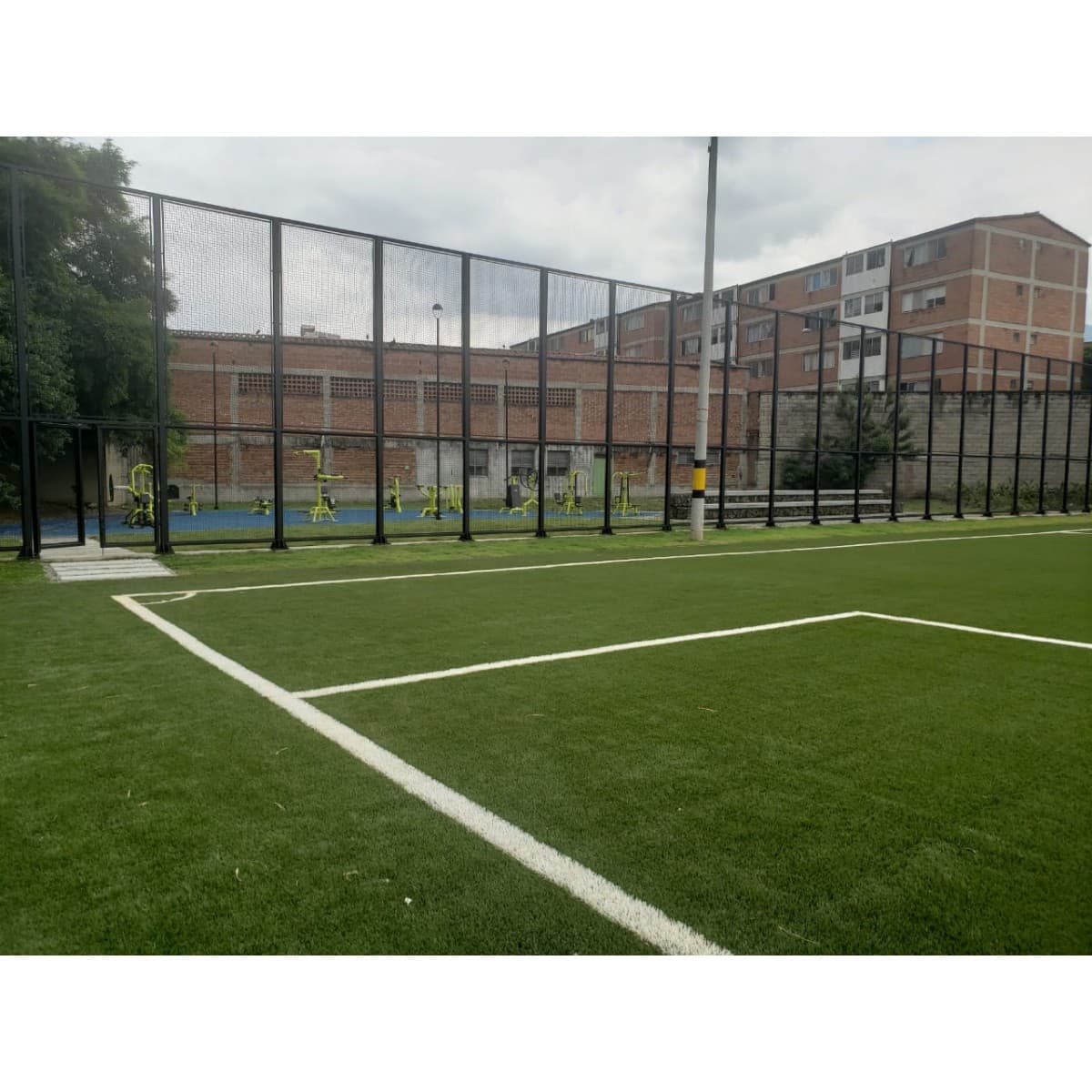 Cancha de fútbol con grama sintética y línea blanca de demarcación, cerrada con malla