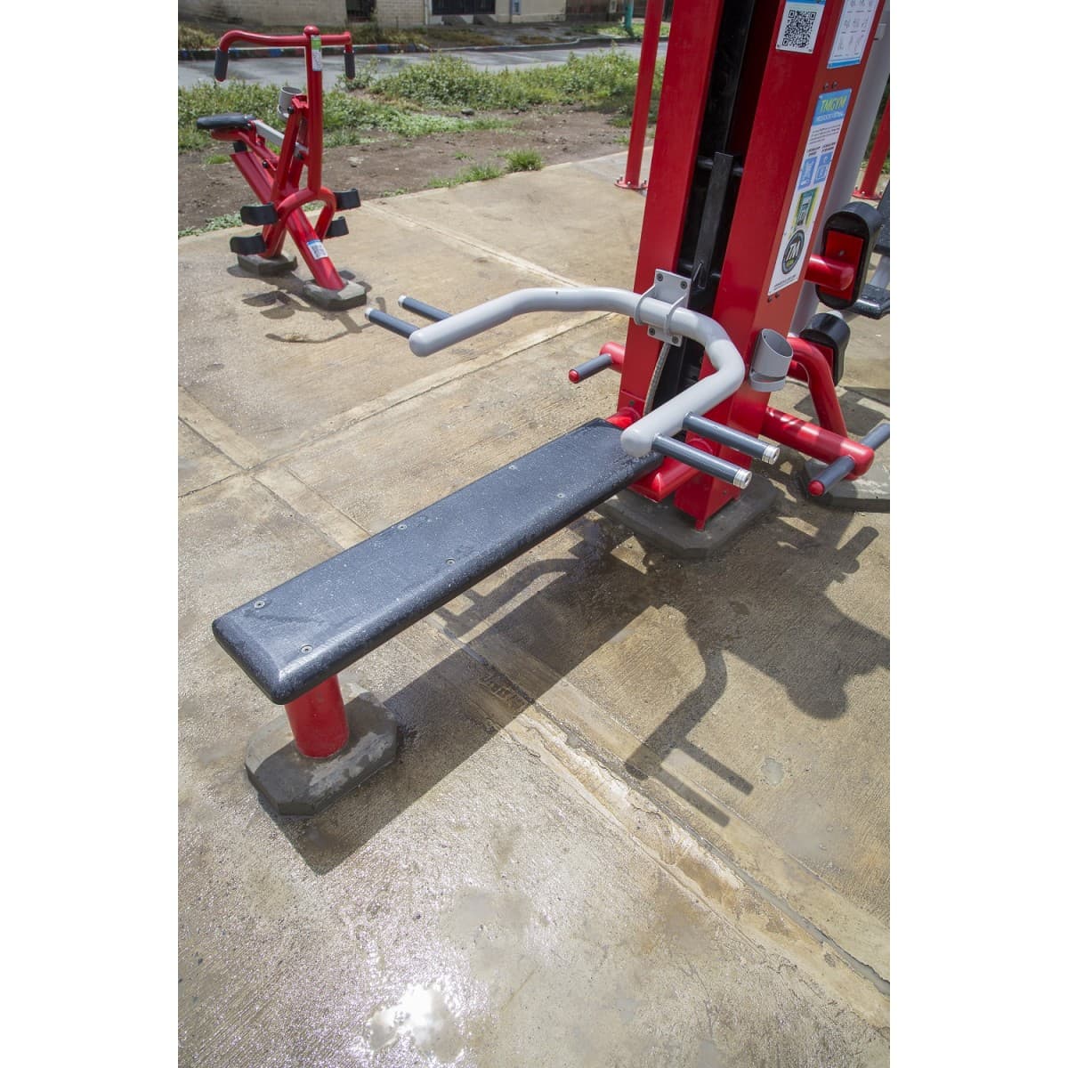 Torre de pecho de 100 libras de TMGYM con banca plana, equipo rojo y negro sobre concreto en un gimnasio al aire libre