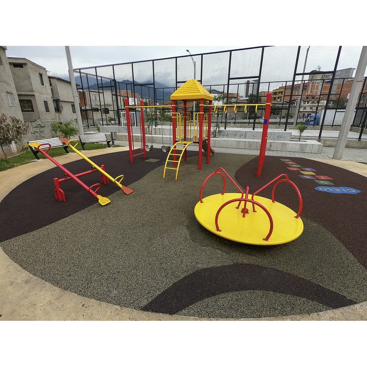Parque infantil recreativo metálico con carrusel, balancines y juegos de estructura roja sobre piso oscuro